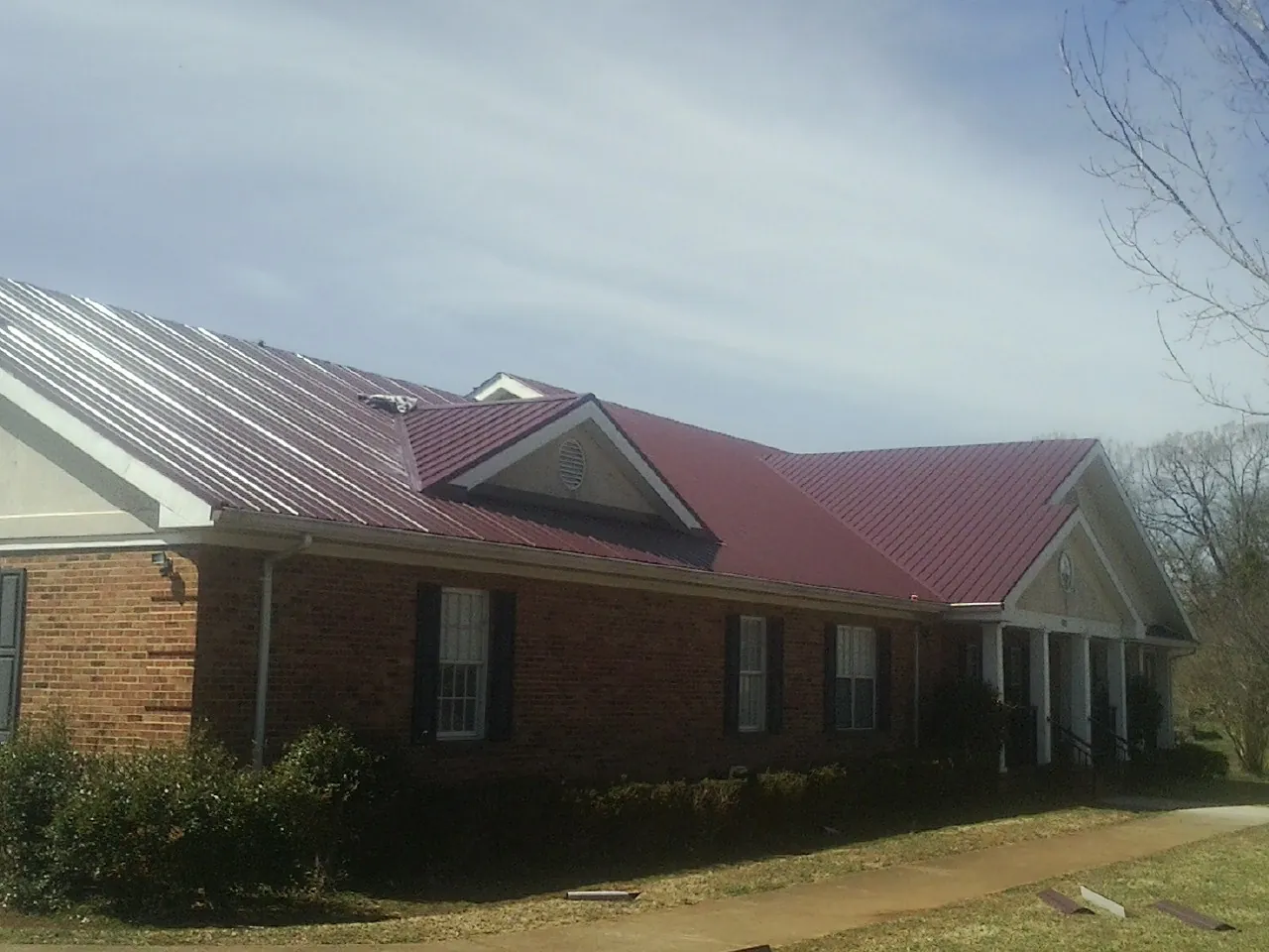 Red metal roof with gabled entries on a long brick building, from a Hail Damage Roof Repair job in Milner