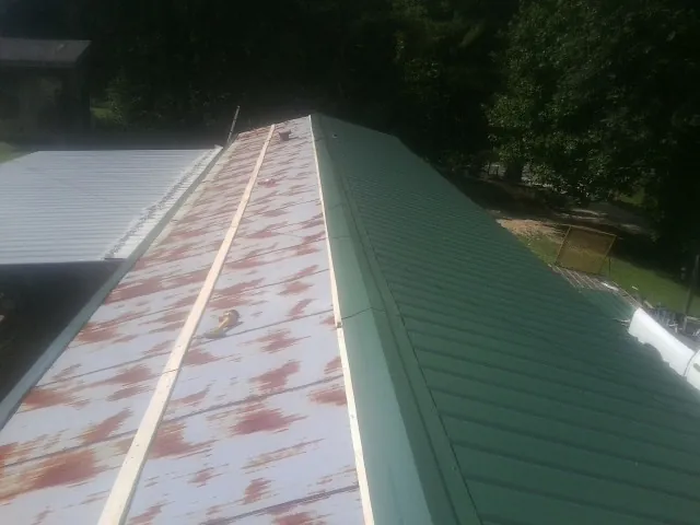 Old rusted panels beside newly installed green metal roofing — Wind Damage Roof Repair by Roofing Brothers in Milner