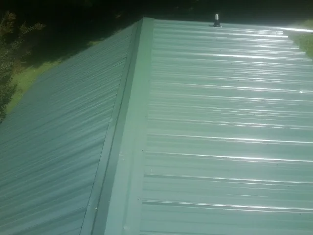 New green metal panels meeting at the ridge of a roof — Flat Roof Repair work by our crew in Milner