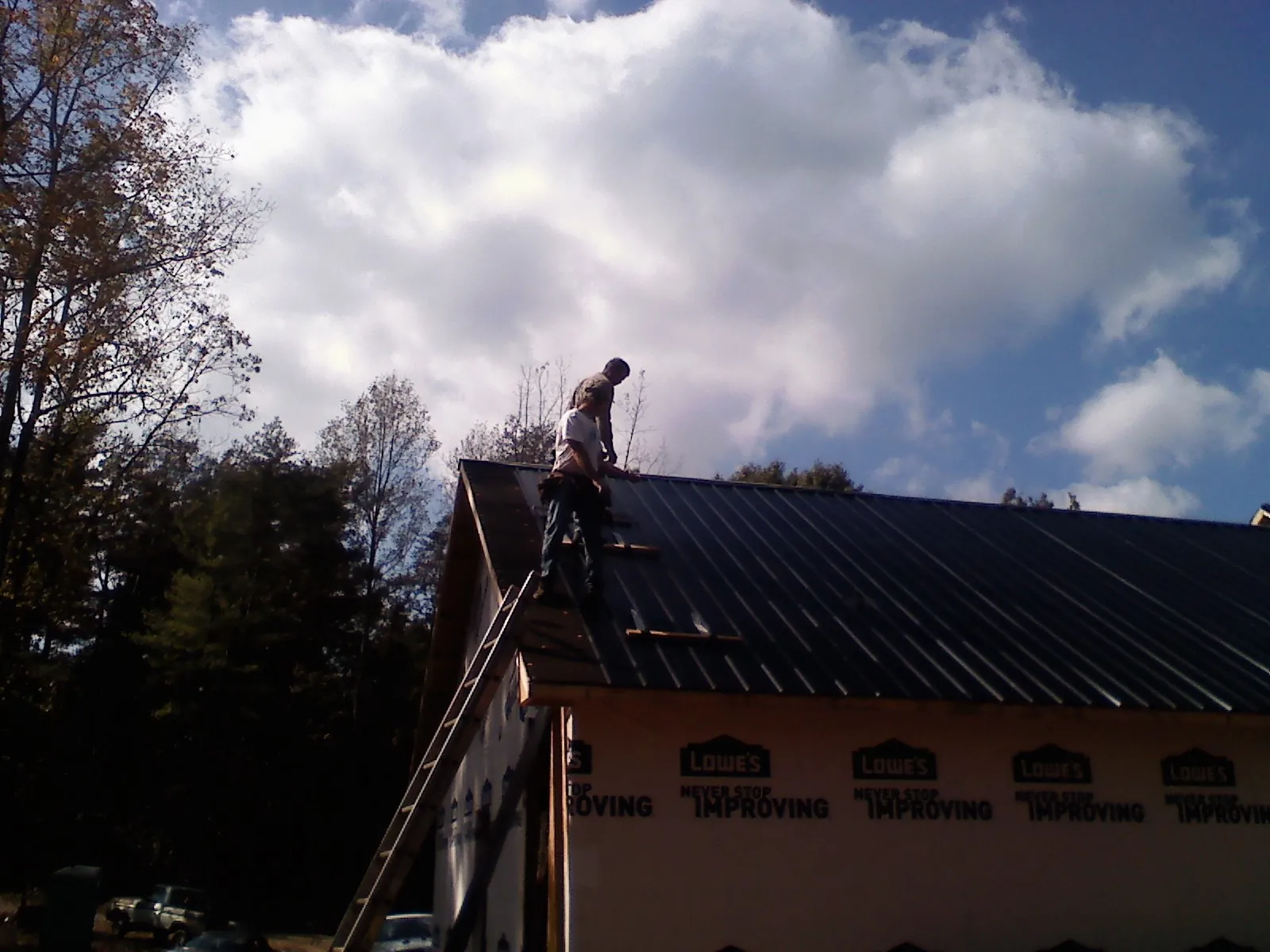 Roofer fastening dark metal panels high against a cloudy sky, from a Roof Inspection job in Milner