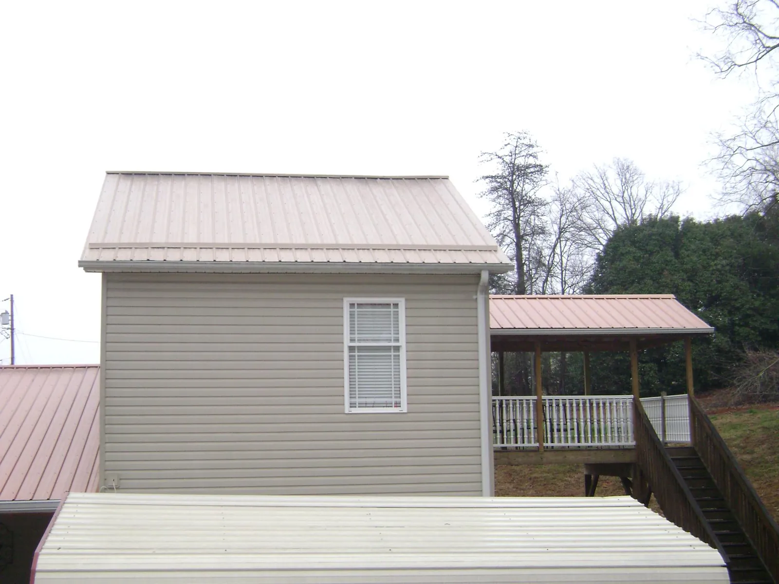 Tan metal roofs on a two story addition and attached porch, from a Roof Replacement job in Milner